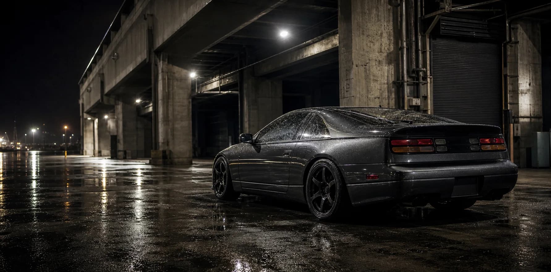 Graphite 1990s-inspired coupe parked beneath an industrial pier after rain